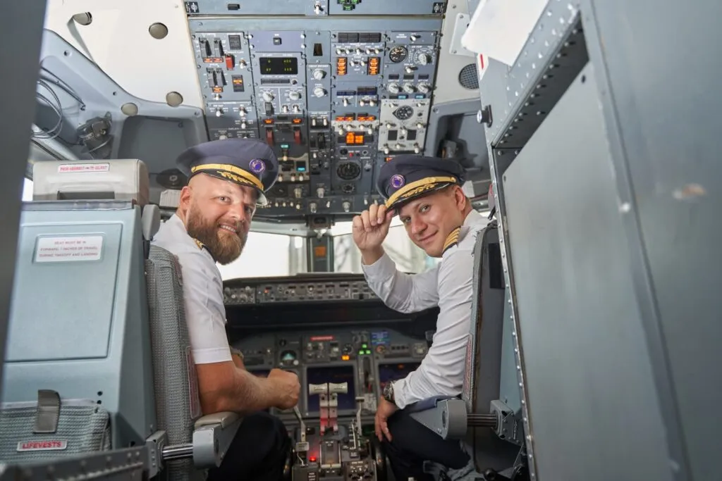 Two pilots smiling and posing in the cockpit, ready for flight.